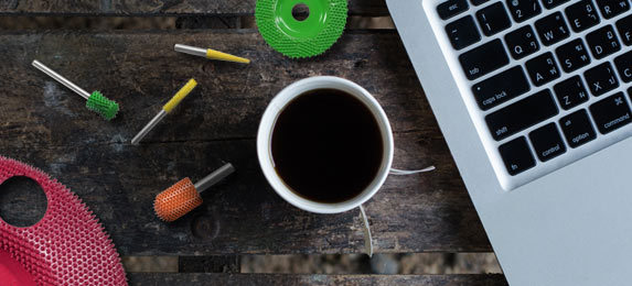 A woodworking workspace with power carving tools, a cup of coffee, and a laptop.